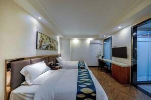 Habitación de hotel con dos camas, un escritorio, un televisor y un ventanal grande.