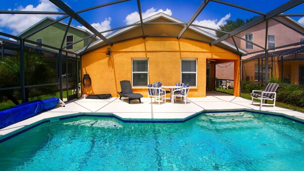 Una piscina con un patio coperto, una sedia e un tavolo.