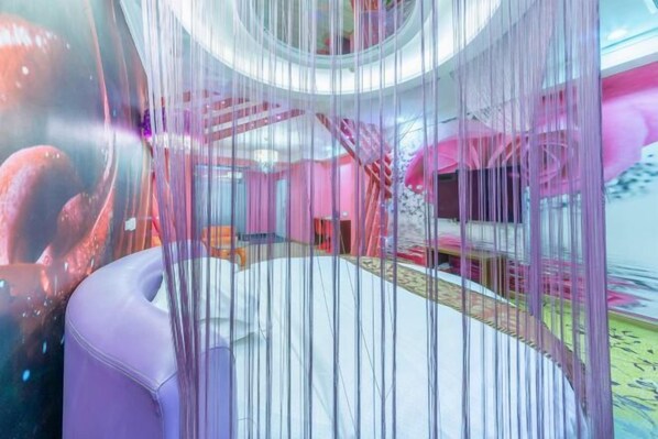 A modern hotel room with a circular bed, a pink staircase, and a large window.