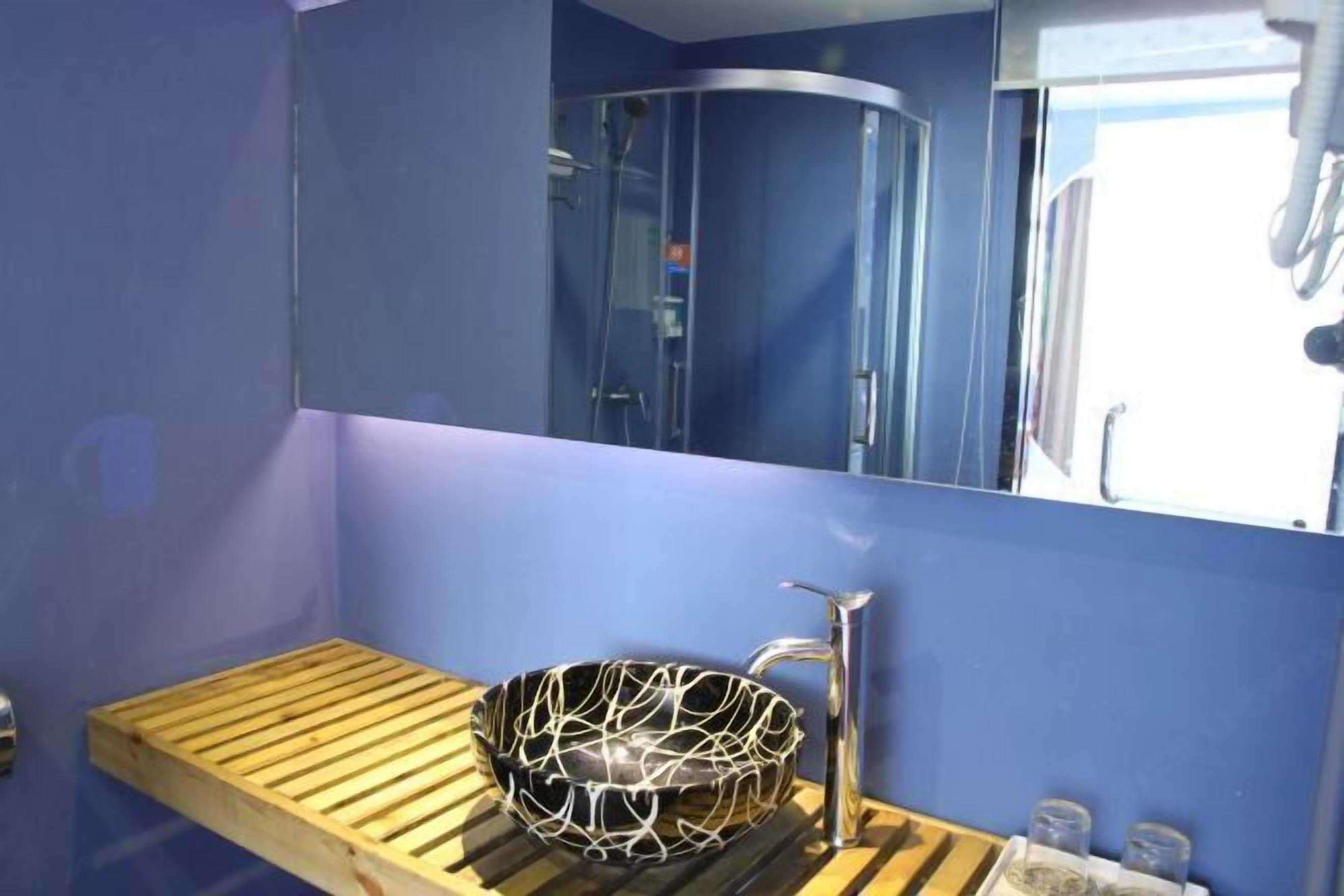 A bathroom with a wooden vanity, a black and white patterned basin, a chrome faucet, and a mirror reflecting a shower area.