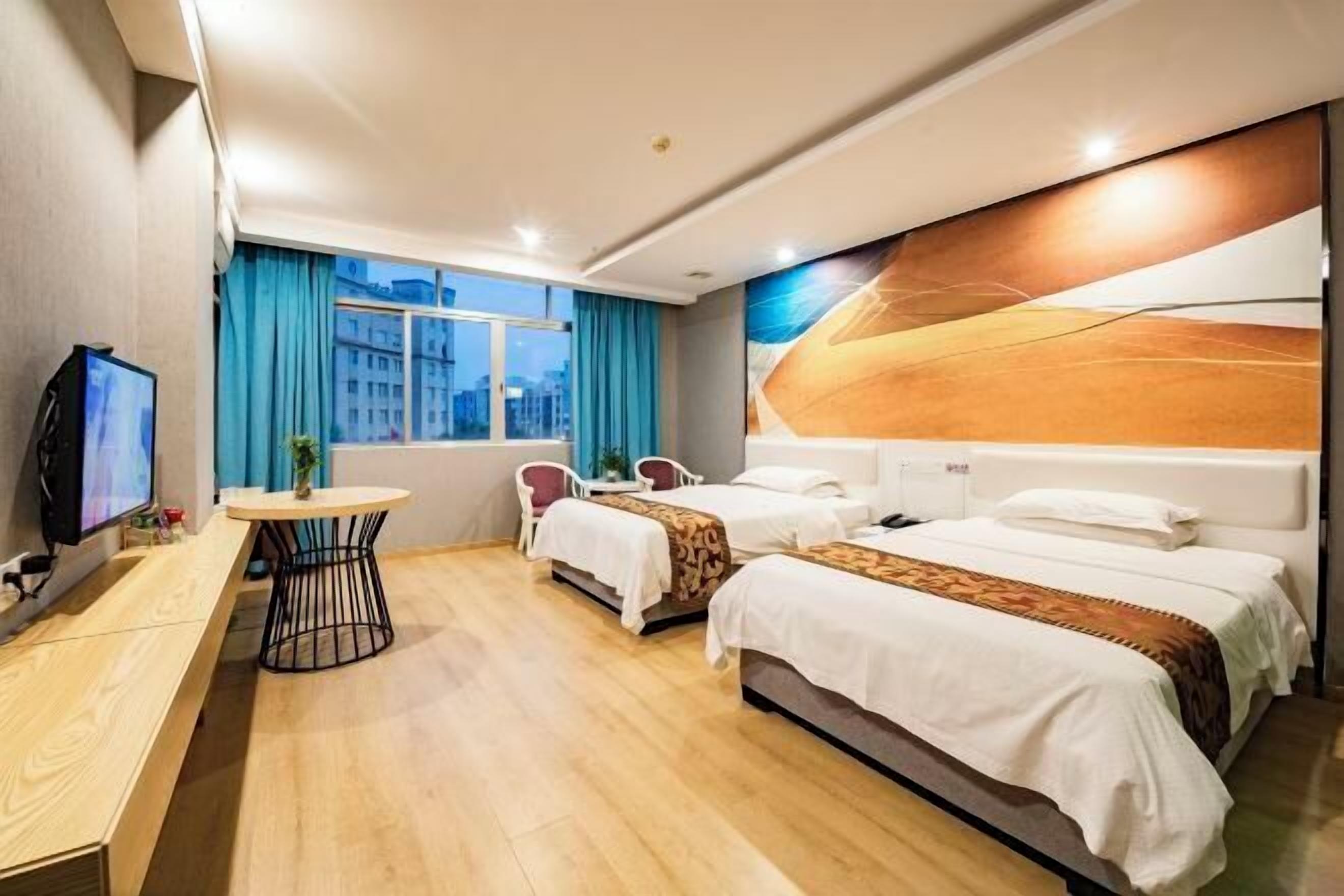 Quarto de hotel com cama, escrivaninha, cadeira, televisão e janela com cortinas.