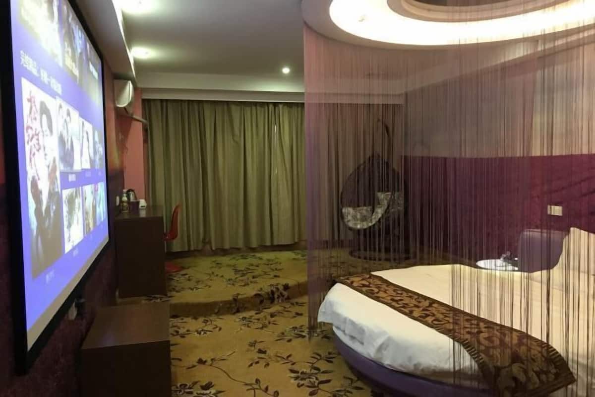 A hotel room with a bed, a TV screen displaying images, a curtain, and a patterned carpet.