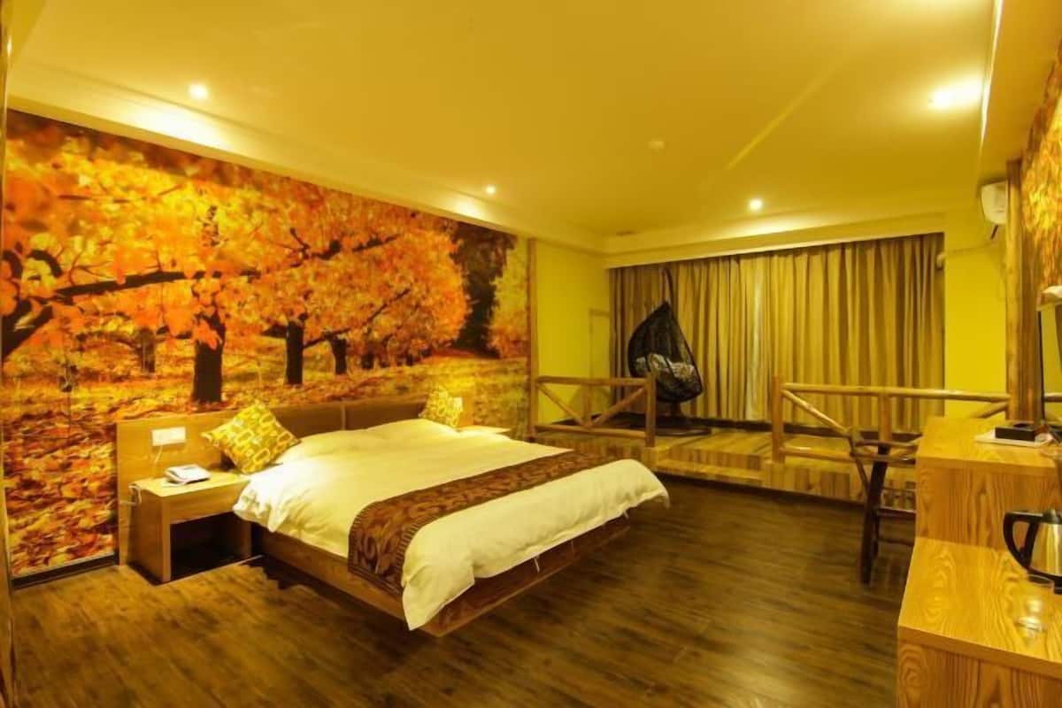 A bedroom with a large bed, a desk, and a chair. There is a wall mural of autumn leaves.
