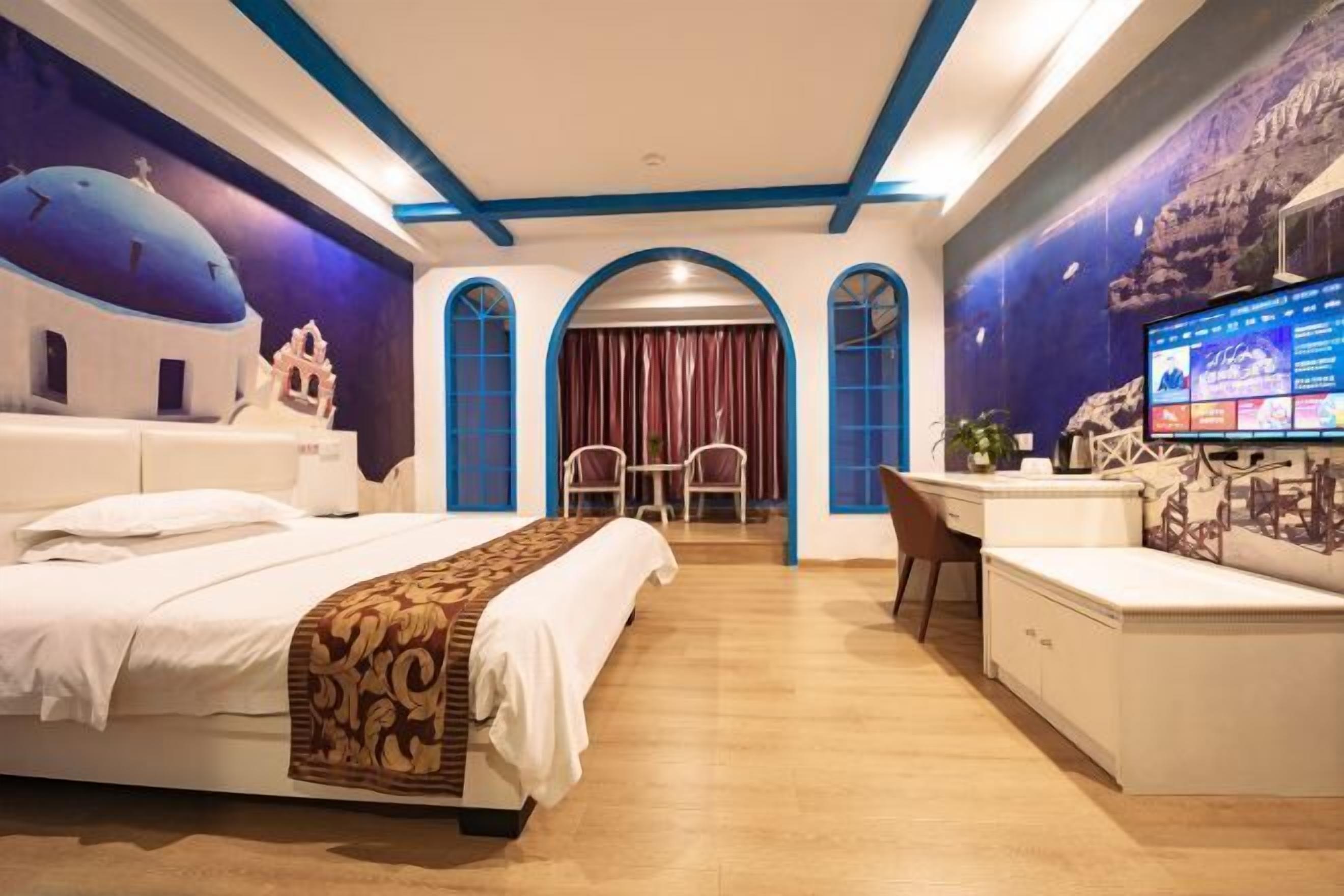 A hotel room with a bed, desk, and TV. There are arched windows and a mural on the wall.