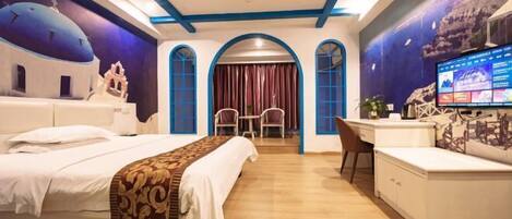 A hotel room with a bed, desk, and TV. There are arched windows and a mural on the wall.