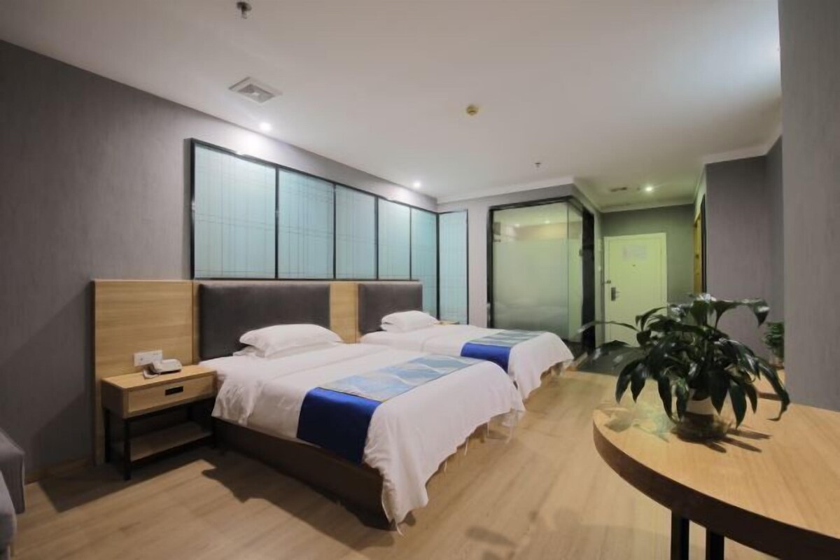 A hotel room with two beds, a bedside table with a phone, a round wooden table, and a potted plant.