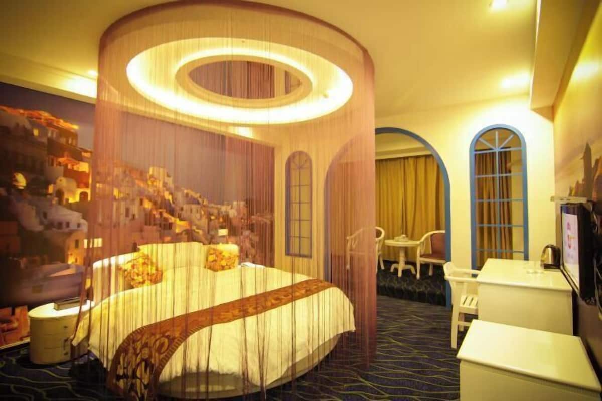 A hotel room with a large bed, a desk, and a chair. There are curtains and a window.