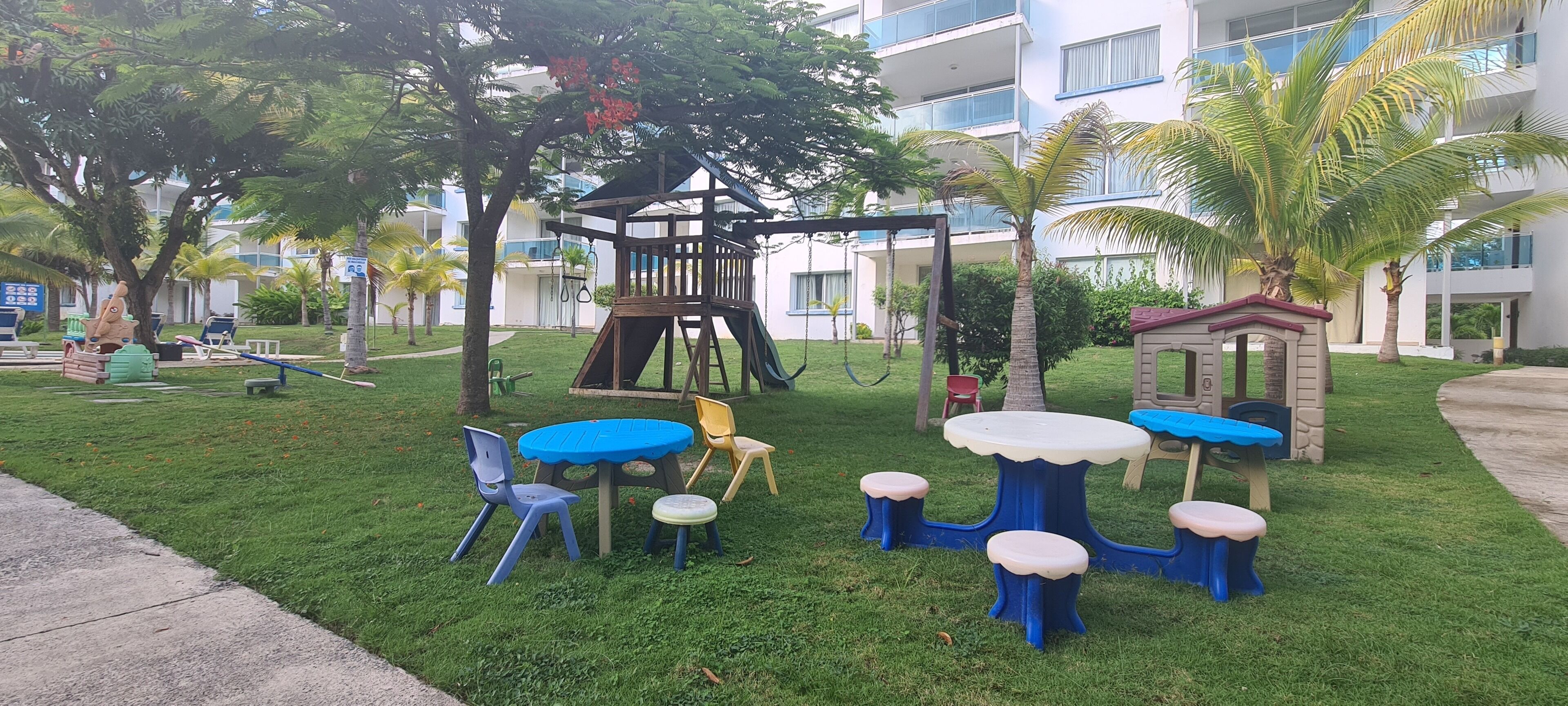 Un espace de jeux pour enfants comprenant une balançoire, une petite structure en bois et une table avec des chaises.