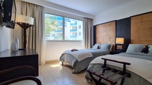 Una camera d'albergo con due letti, una scrivania, una sedia, una lampada e vista sugli edifici dalla finestra.