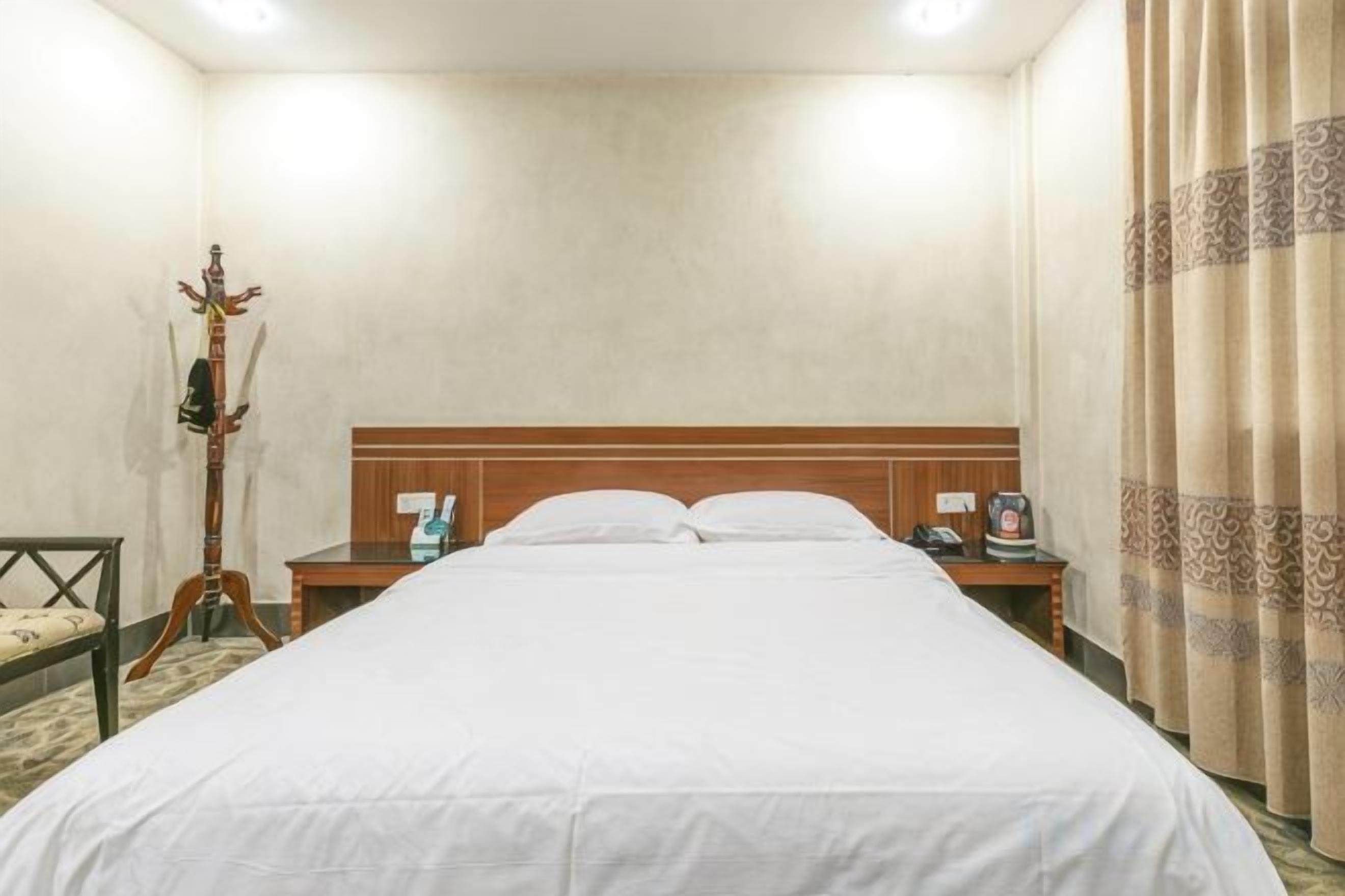 A hotel room with a large bed, a wooden headboard, a nightstand with a lamp, and a coat stand.