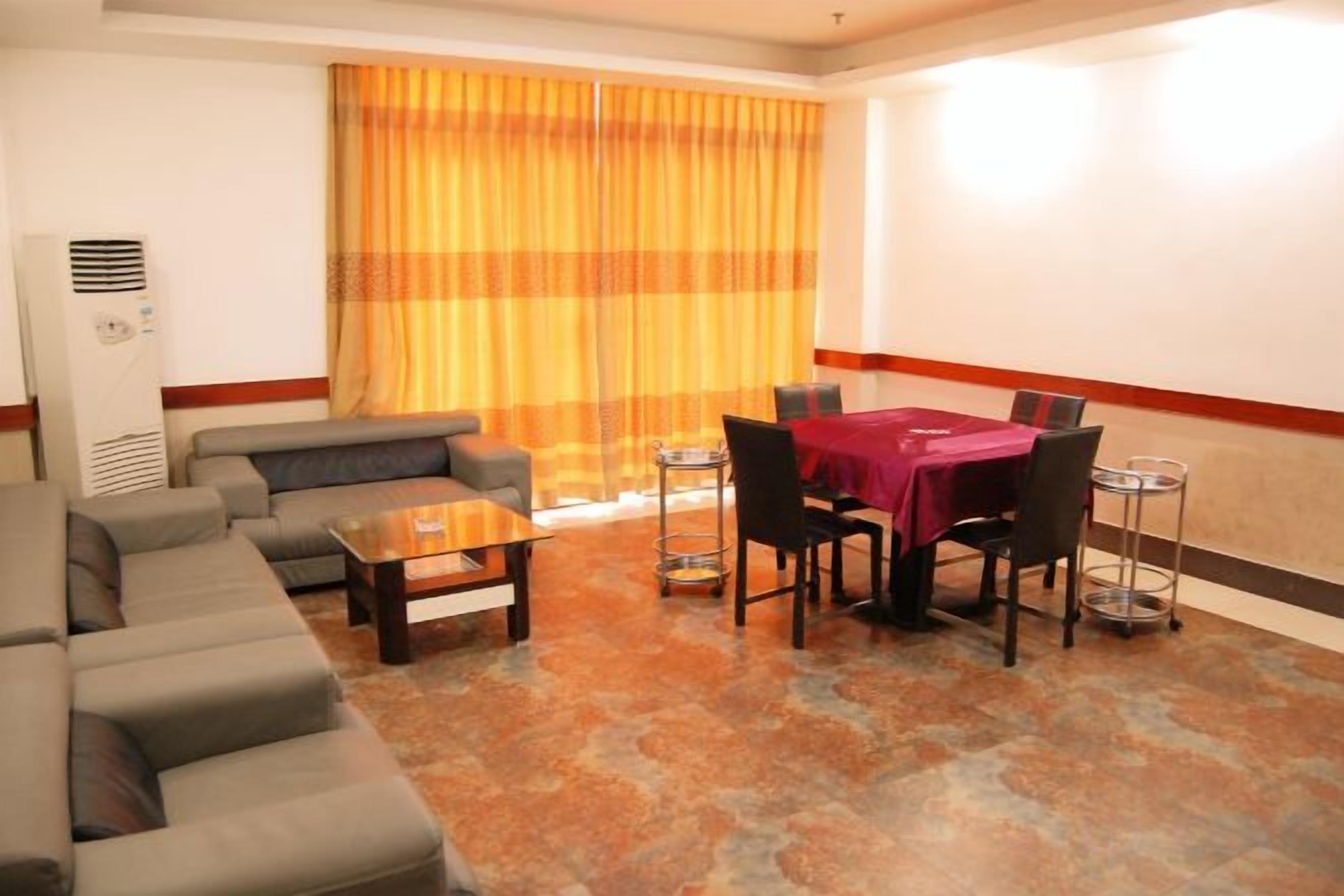 A hotel room with a sofa set, a dining table with chairs, and a large window with curtains.