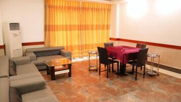 A hotel room with a sofa set, a dining table with chairs, and a large window with curtains.