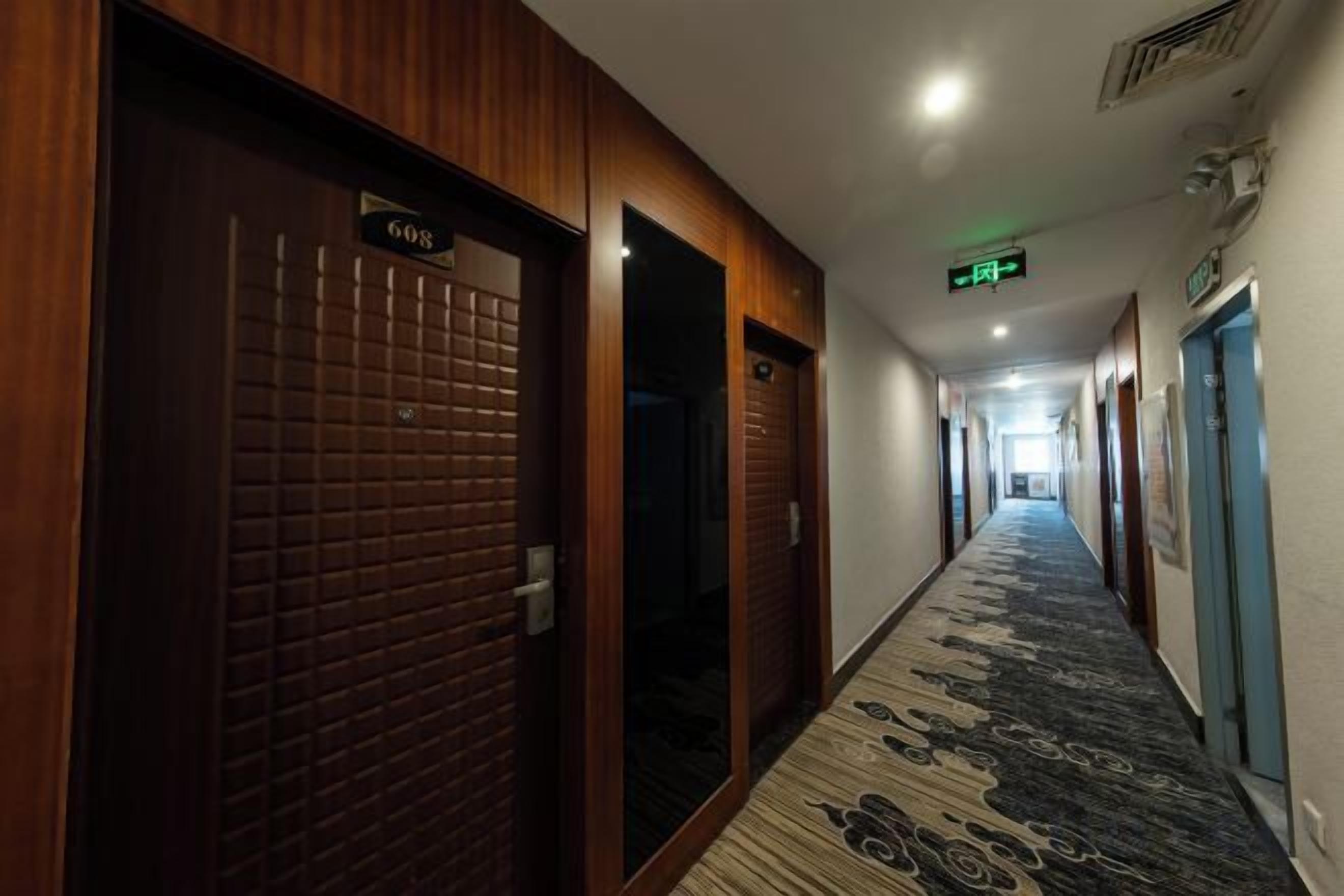 Corredor de hotel com portas de madeira, carpete estampado e sinal de saída.
