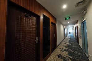 A hotel corridor with wooden doors, a patterned carpet, and an exit sign. - Jiangmen Baiwo Hotel (Wuyi Hospital of Traditional Chinese Medicine West Area) (Jiangmen)