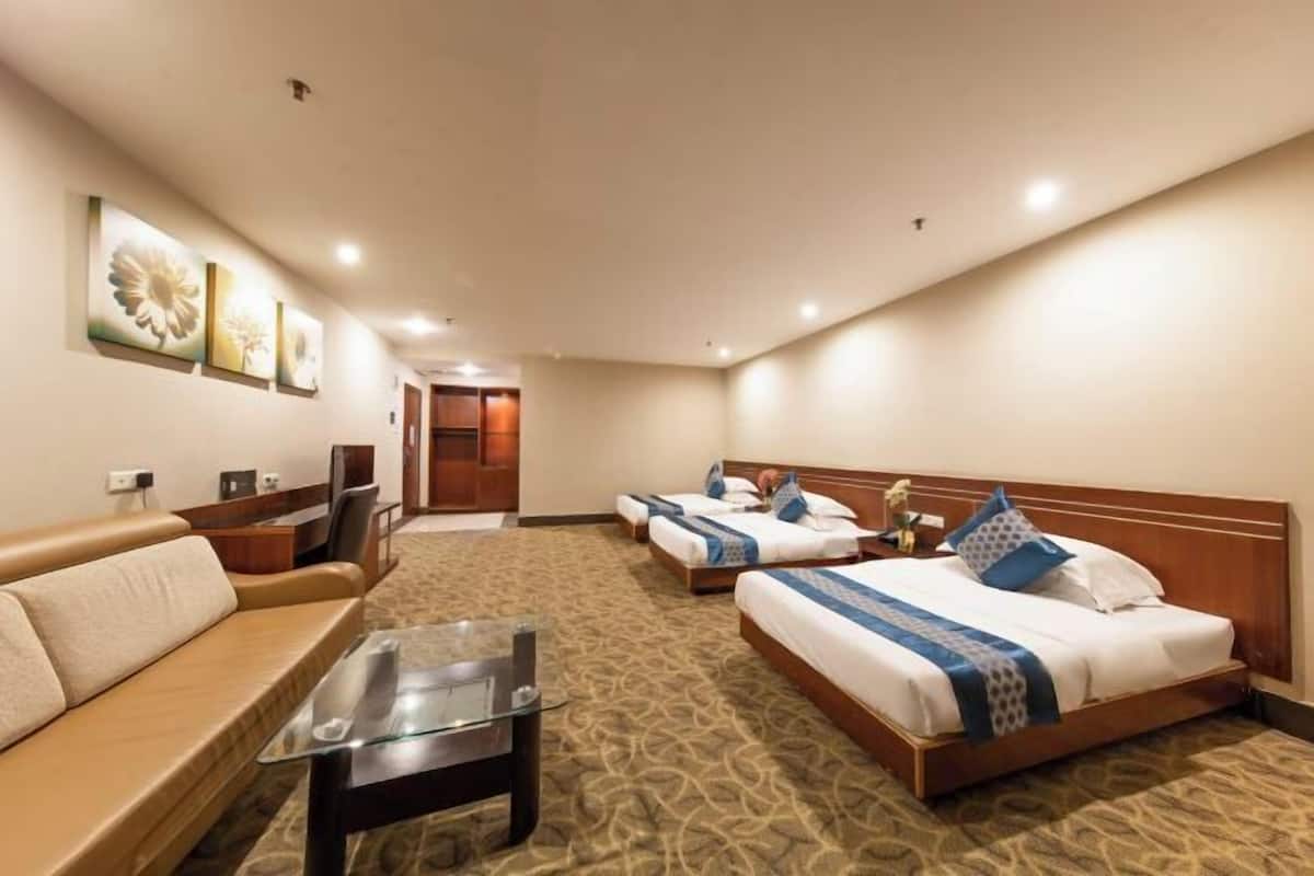Una habitación de hotel con sofá, una mesita de centro de cristal, dos camas individuales, cabecero de madera y suelo alfombrado.