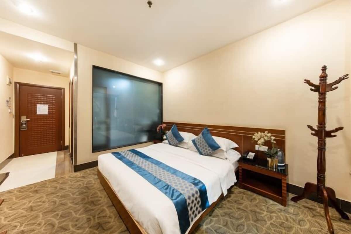 Habitación de hotel con una cama grande, una mesita de noche de madera, un perchero y una puerta con ventanal.