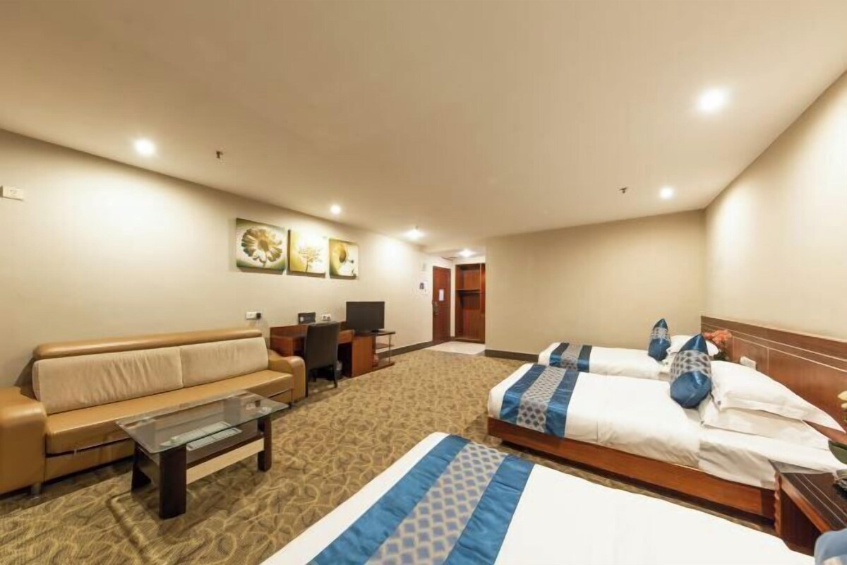 Ein Hotelzimmer mit zwei Betten, einem Sofa, einem Schreibtisch und einem Fernseher.