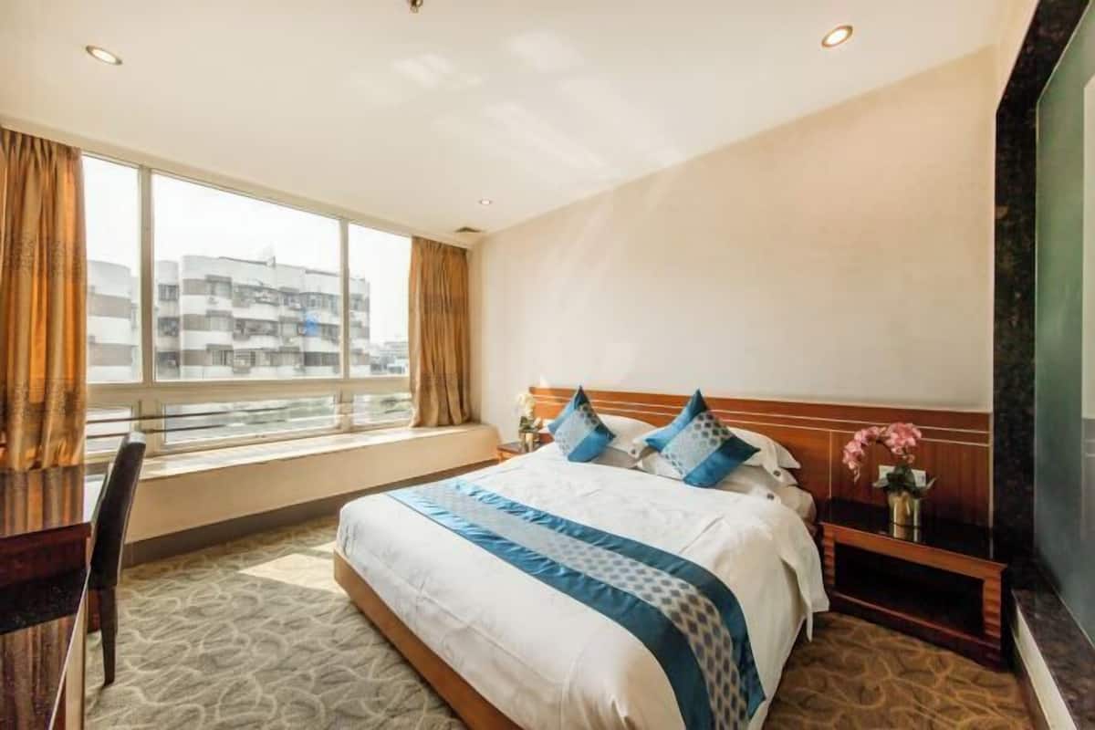 Una habitación de hotel con una cama grande, una mesita de noche, una silla y un ventanal con cortinas.