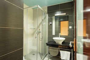 A modern bathroom with a glass-enclosed shower, a white sink, and dark tiled walls. - Jiangmen Baiwo Hotel (Wuyi Hospital of Traditional Chinese Medicine West Area) (Jiangmen)