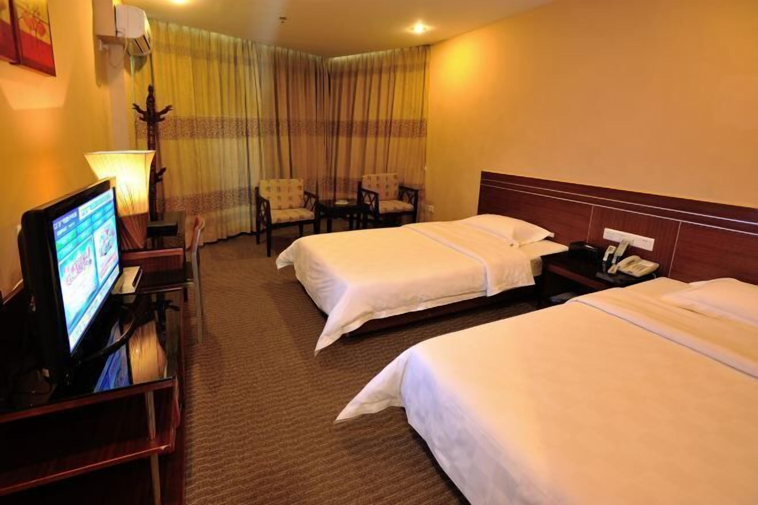 A hotel room with two beds, a desk with a TV, and a chair.