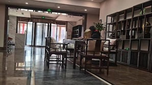 A lobby with a marble floor, wooden chairs, a reception desk, and a bookshelf with decorative items. - Hancun River Villa (Beijing)