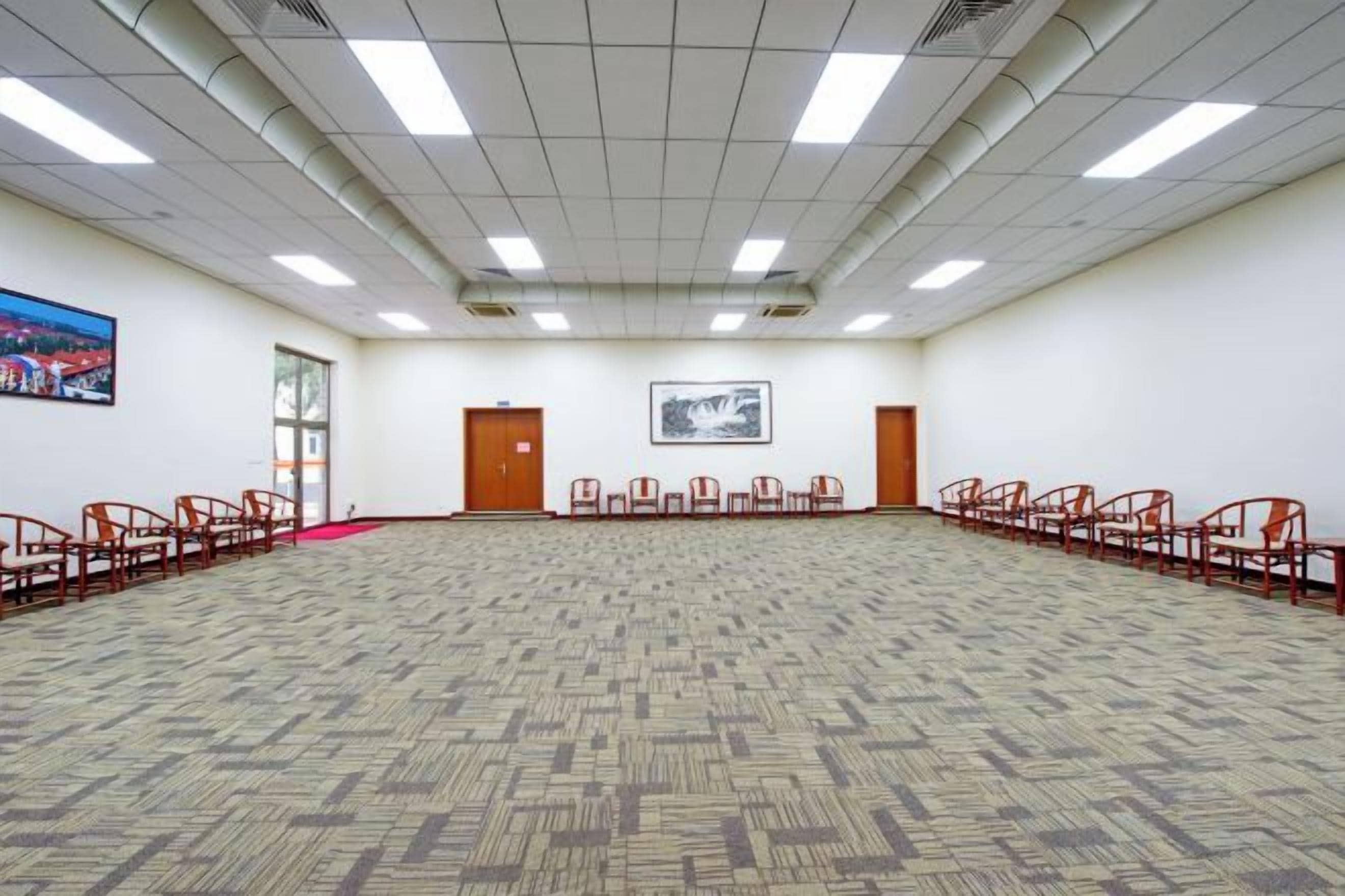Un amplio salón de conferencias con alfombra estampada, filas de sillas e iluminación fluorescente en el techo.