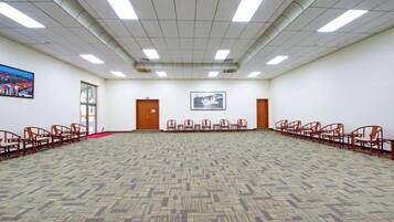 Un amplio salón de conferencias con alfombra estampada, filas de sillas e iluminación fluorescente en el techo.