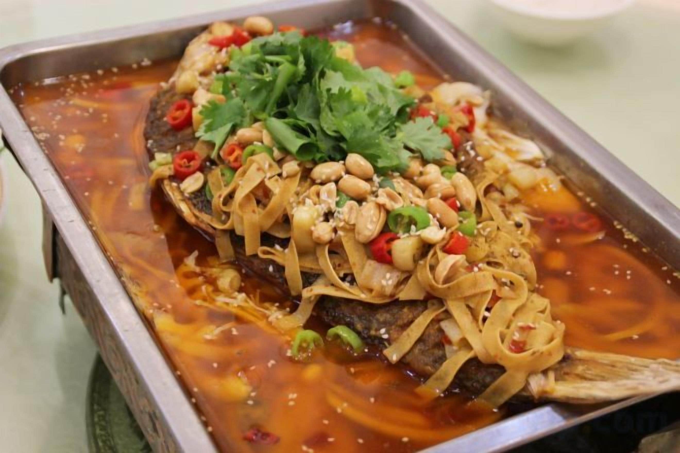 Un plat de poisson, servi sur un plateau et agrémenté de cacahuètes, de piment rouge et de coriandre.