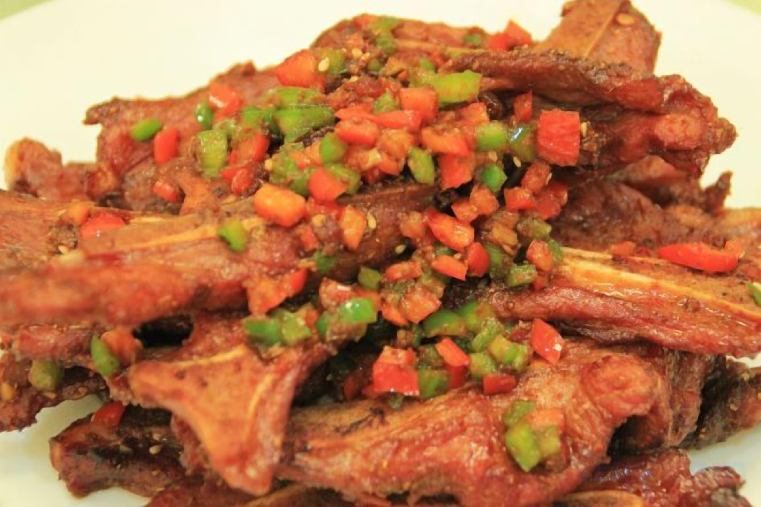 A plate of cooked meat with a garnish of diced vegetables.