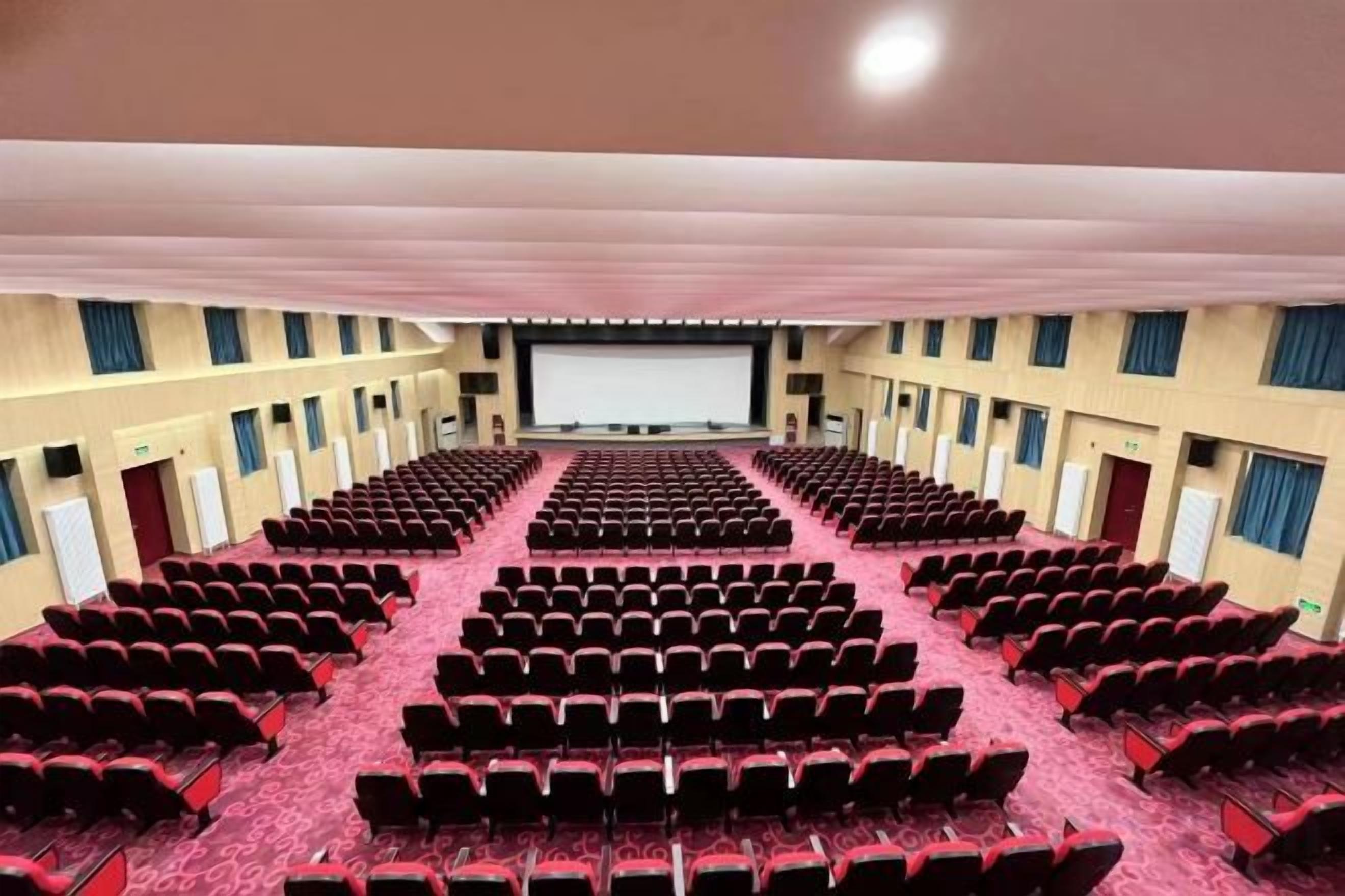 A large indoor auditorium with rows of seats, a stage at the front, and a balcony.