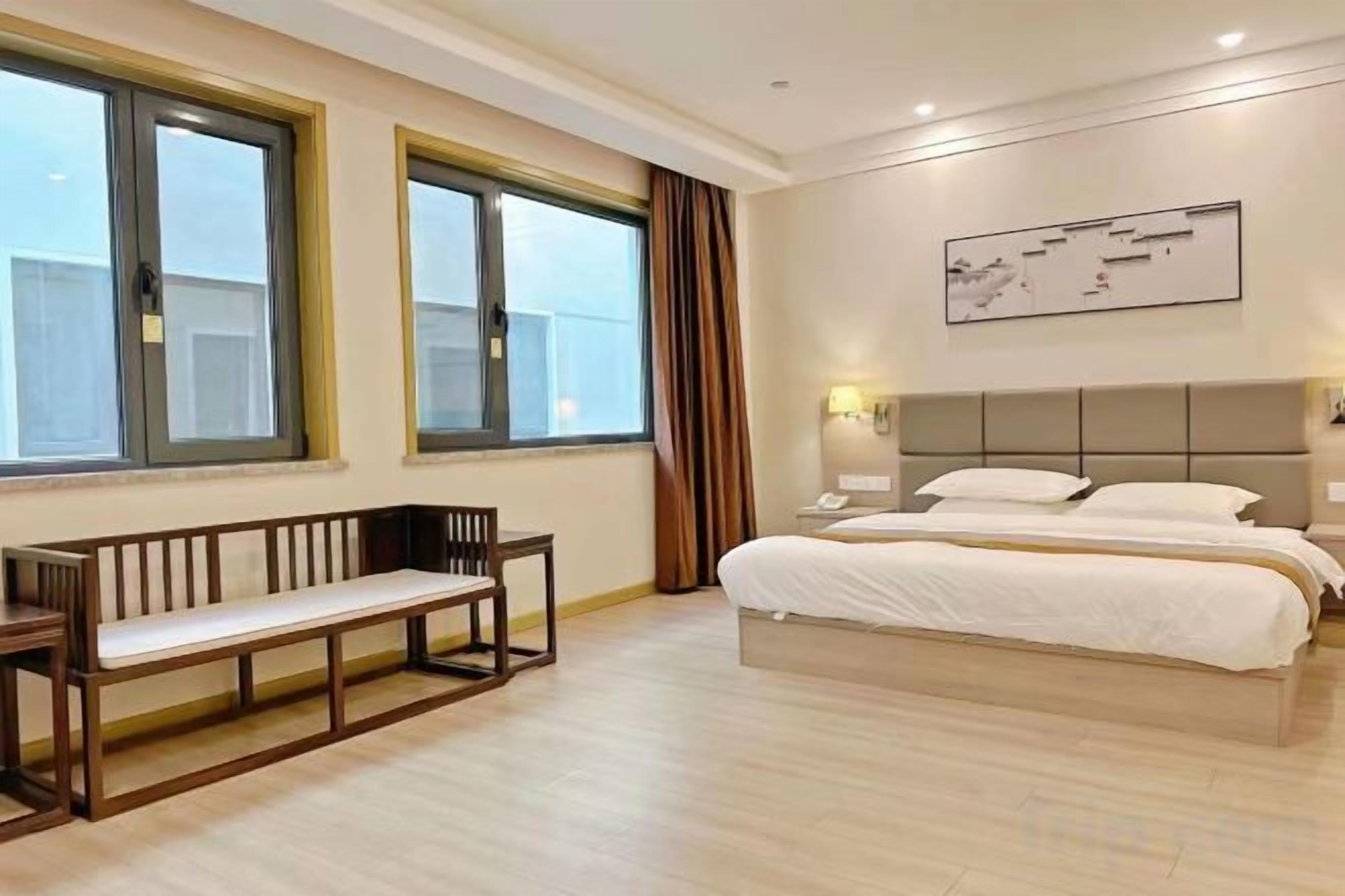 A hotel room with a bed, a bench, and large windows.