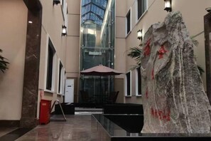 A lobby with a glass atrium, seating area, and a stone sculpture. - Hancun River Villa (Beijing)
