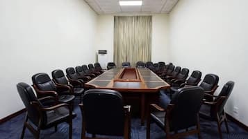 Sala de conferências com uma mesa comprida rodeada de cadeiras, piso coberto por carpete e uma cortina ao fundo.