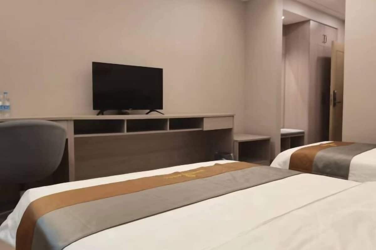 A hotel room with two beds, a TV, a desk, and a wardrobe.