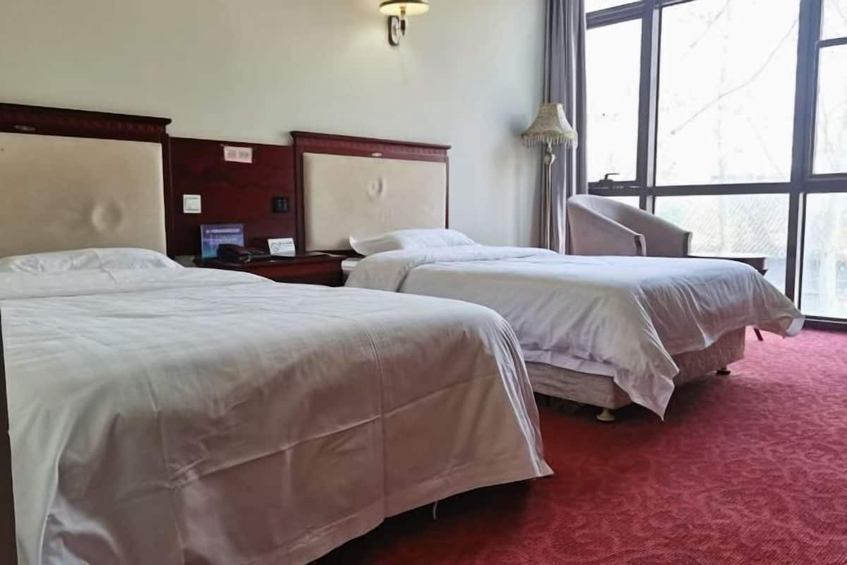 A hotel room with two beds, a desk, a lamp, and a large window.