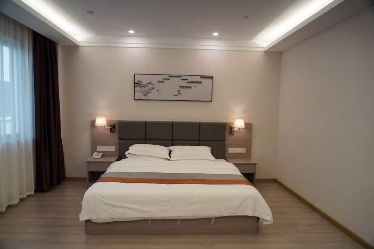 A hotel room with a large bed, two bedside tables with lamps, a headboard, and a wall-mounted artwork.