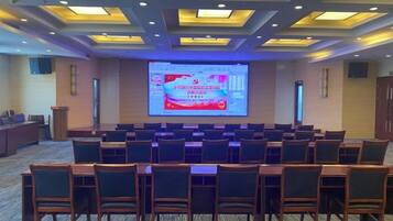 A conference room with rows of chairs facing a large screen displaying a presentation.