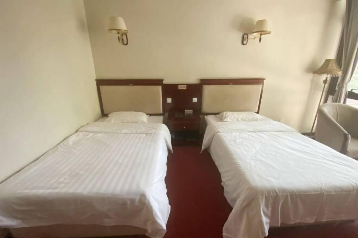 A hotel room with two single beds, a red carpet, and two wall-mounted lamps.