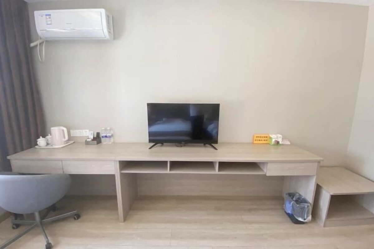 A hotel room with a wooden desk, a television, a chair, and an air conditioning unit.