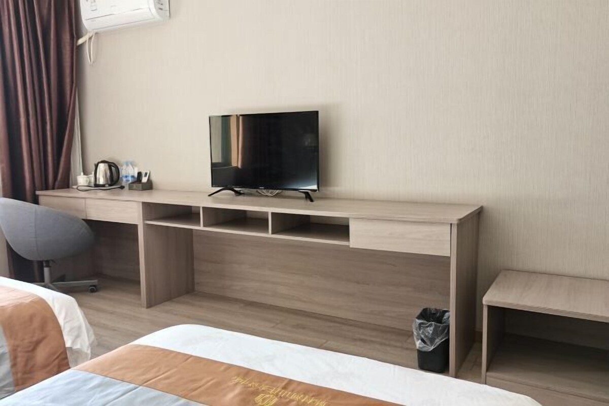 A hotel room with a bed, a desk with a television, a chair, and a trash bin.
