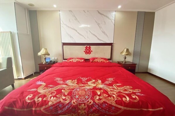 Una habitación de hotel con una cama grande, dos mesitas de noche, un cabecero con un panel decorativo y una ventana con cortinas.