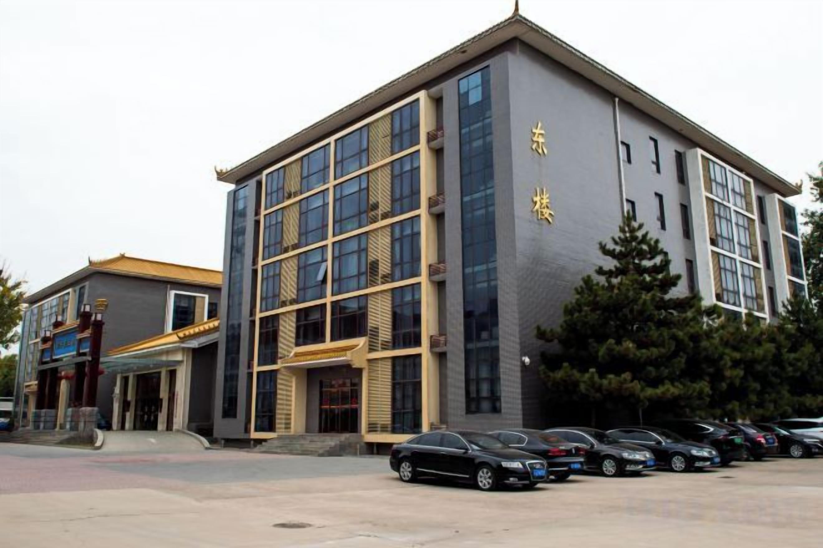 A modern building with a prominent entrance, multiple windows, and a parking area with several cars.