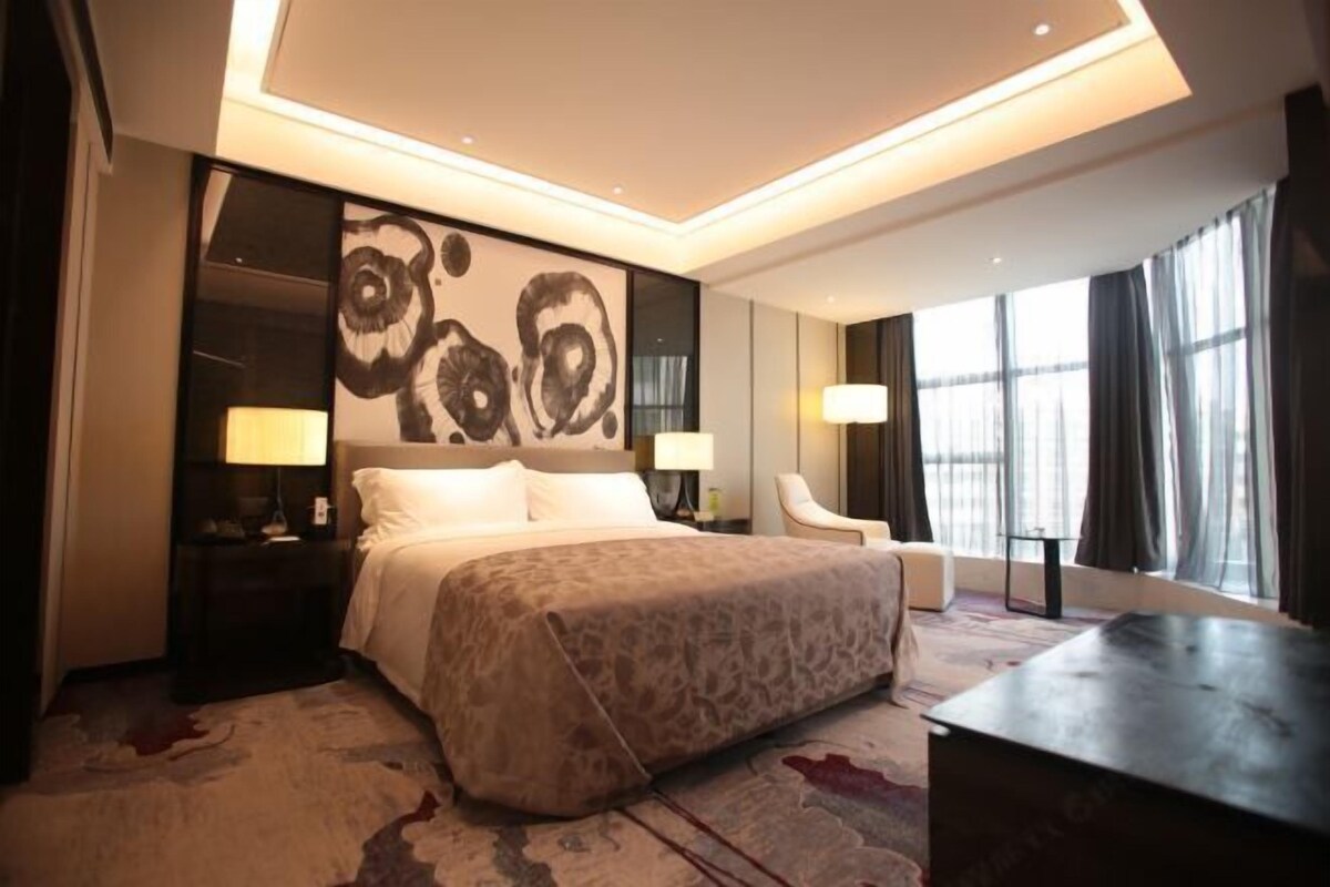 A modern hotel room with a large bed, two bedside tables, a desk, and a chair.