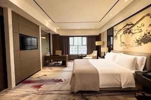 A hotel room with a large bed, a desk, a chair, a TV, and a painting on the wall. - Nature Hotel Four Seasons (Quanzhou)