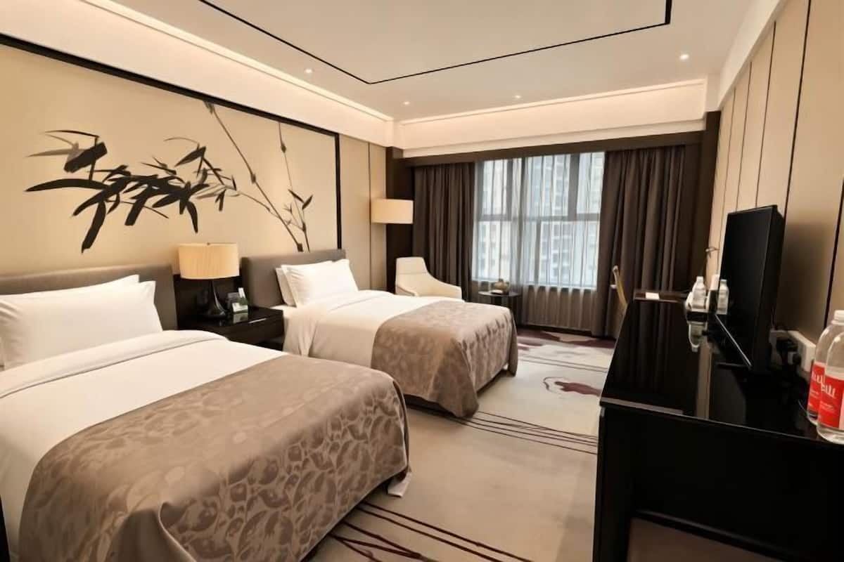 Ein Hotelzimmer mit zwei Betten, einem Fernseher, einem Schreibtisch und einem großen Fenster.