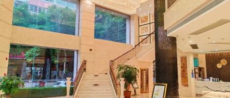A spacious lobby with a grand staircase, large windows, and a reception desk.