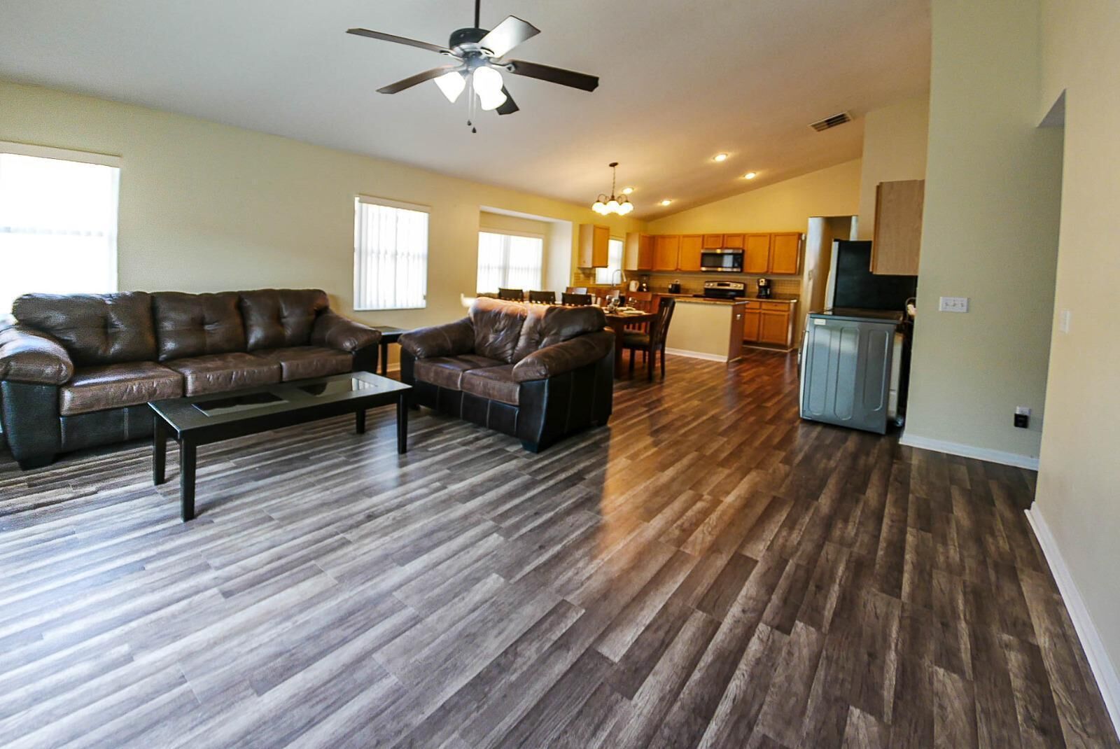 A spacious living room with a dark wood floor, leather sofas, and a ceiling fan.