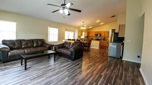 A spacious living room with a dark wood floor, leather sofas, and a ceiling fan. - Beautiful 5/5 Bedroom Home!!! (Davenport)