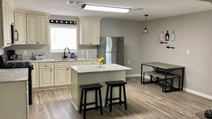A kitchen with white cabinets, a stainless steel refrigerator, a marble countertop, and a small dining area with stools. - Twin Oaks Cozy Getaway in Lake Charles (Lake Charles)