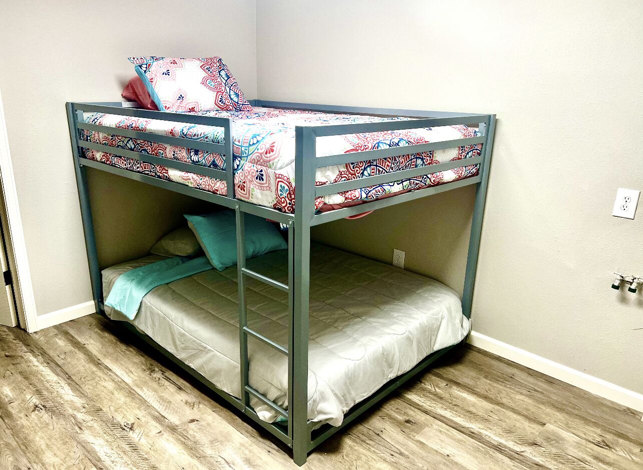 Un letto a castello con una scala, una coperta a motivi e un cuscino color petrolio.